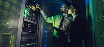 Two professionals in a server room taking notes