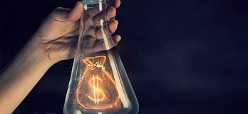 Hand holding a beaker with a glowing money bag inside