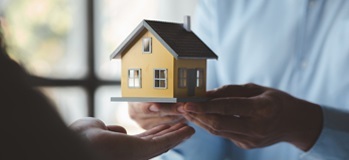 One person handing a model house to another