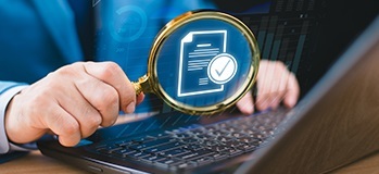 Laptop user holding up magnifying glass to get closer look at employee benefits